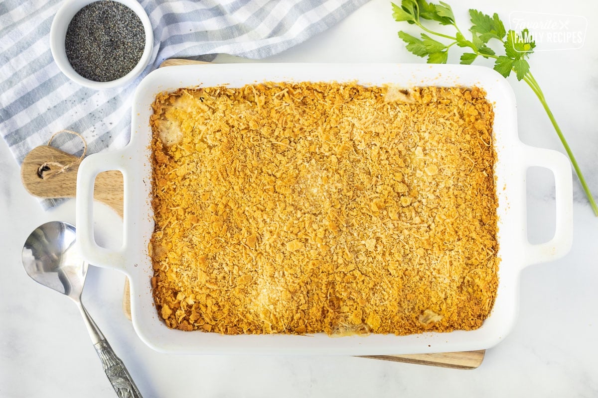 Baking dish with Poppy Seed Chicken. Poppyseeds, parsley and a spoon on the side.