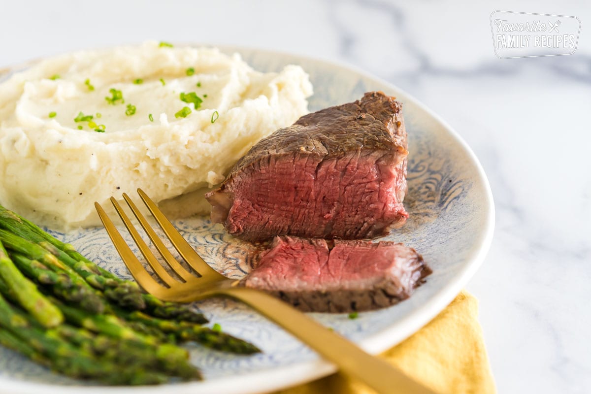 Filet mignon sliced on a plate with mashed potatoes and asparagus.