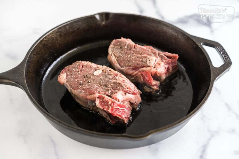 Two uncooked filet mignons in a cast iron pan