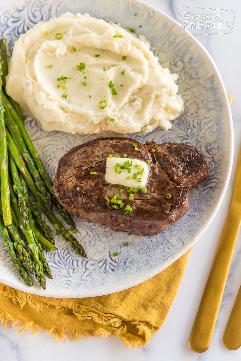 Cast iron filet mignon on a plate with mashed potatoes and asparagus.