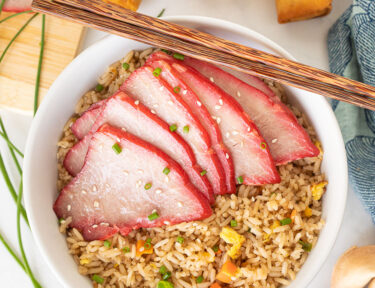 Bowl with fried rice and sliced Char Siu. Spring rolls and fortune cookies on the side.