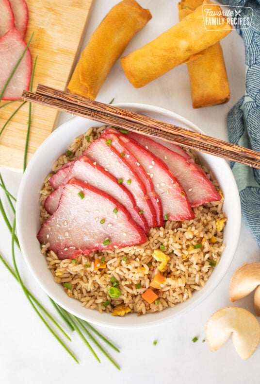 Bowl with fried rice and sliced Char Siu. Spring rolls and fortune cookies on the side.