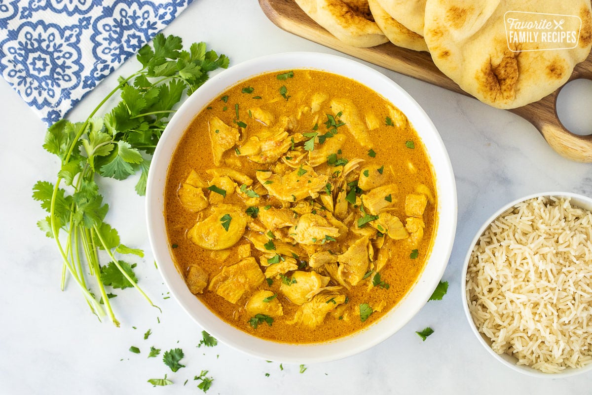 Large bowl of Chicken Korma with Naan bread, cilantro and rice on the side.