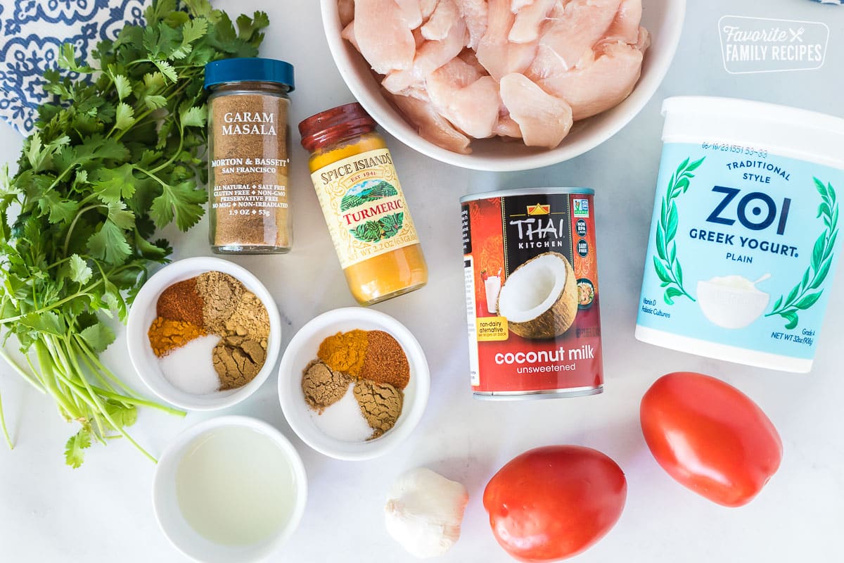 Ingredients to make Chicken Korma including coconut milk, greek yogurt, tomatoes, spices, sliced chicken breast, cilantro, oil and garlic.