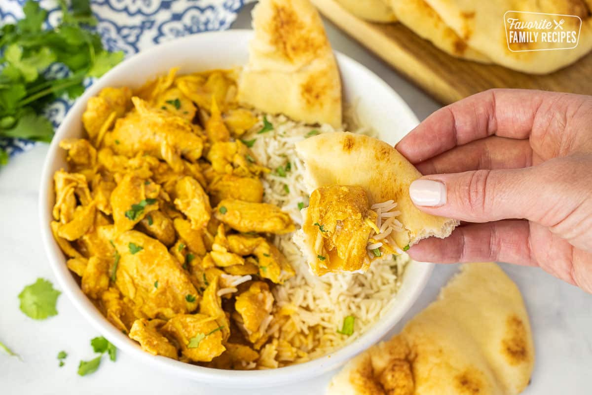 Hand holding a piece of Naan bread with Chicken Korma on top.