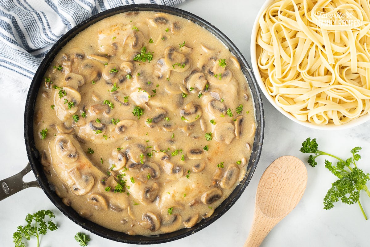 Skillet with Chicken Marsala next to a large bowl of cooked fettuccine pasta.