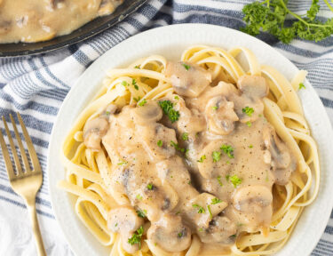 Plate of Chicken Marsala over pasta next to the skillet.