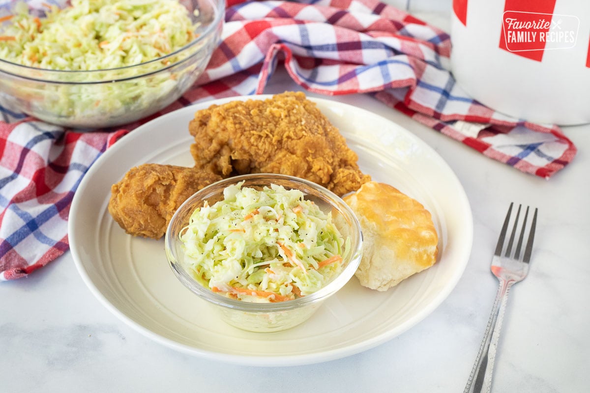 Plate with crispy chicken, biscuit and a small bowl of Coleslaw. Fork on the side.