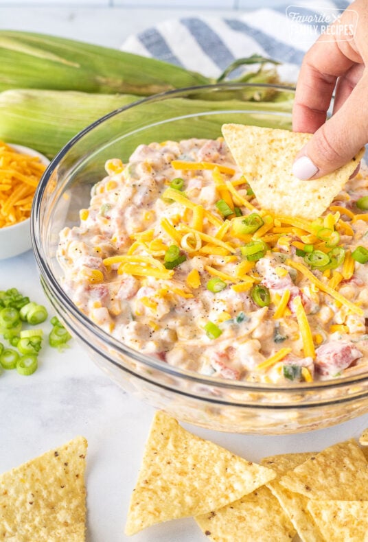 Hand holding a tortilla chip and dipping it into a bowl of Creamy Corn Dip.