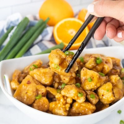 Chopsticks grabbing a piece of Orange Chicken.