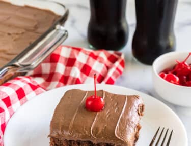 Coca cola cake on a plate topped with a maraschino cherry