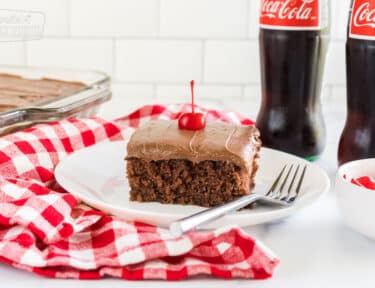 Coca cola cake on a plate topped with a maraschino cherry