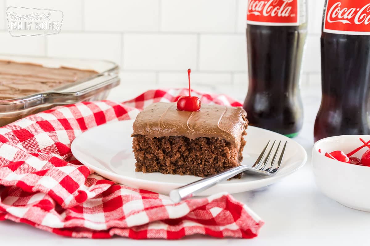 Coca cola cake on a plate topped with a maraschino cherry.