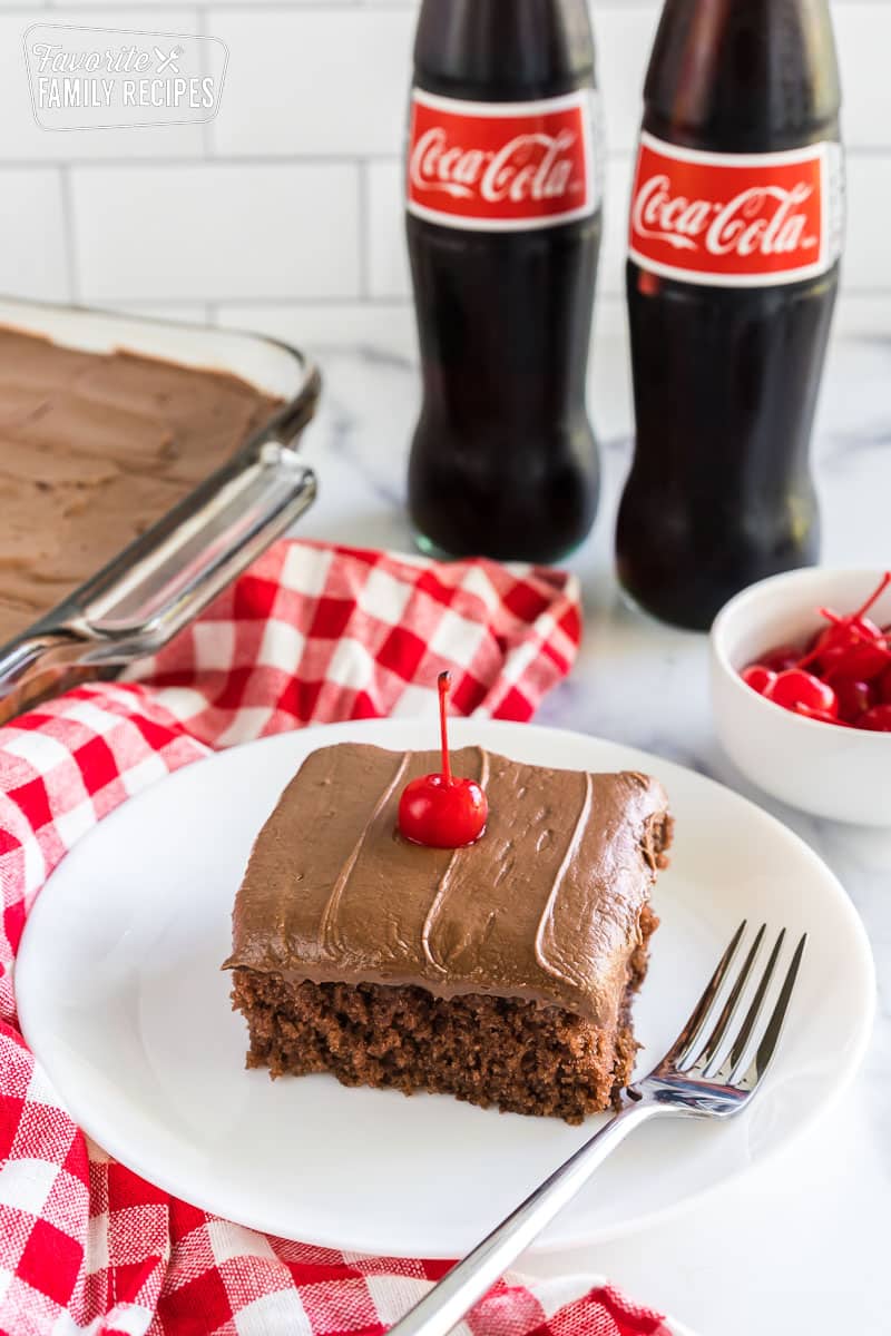 Coca cola cake on a plate topped with a maraschino cherry.