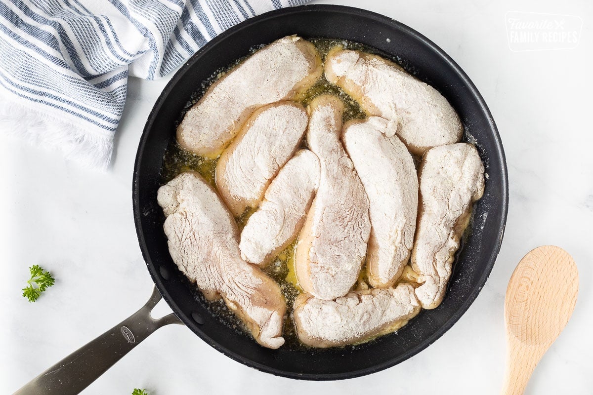 Skillet with oil, butter and pieces of chicken coated in flour for Chicken Marsala.