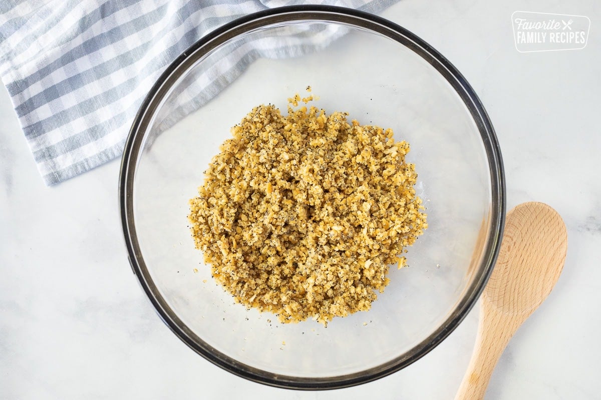 Bowl of butter, poppy seed and crushed Ritz crackers mixture. Wooden spoon on the side.