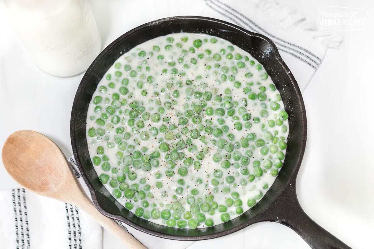 A skillet with creamed peas and topped with cracked black pepper