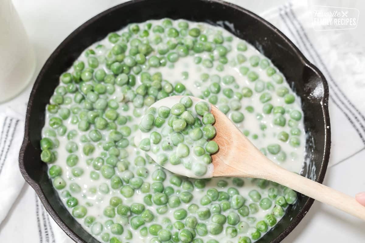 A wooden spoon with a scoop of creamed peas