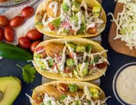 Three Easy Fish Tacos with toppings lined up on a taco stand.