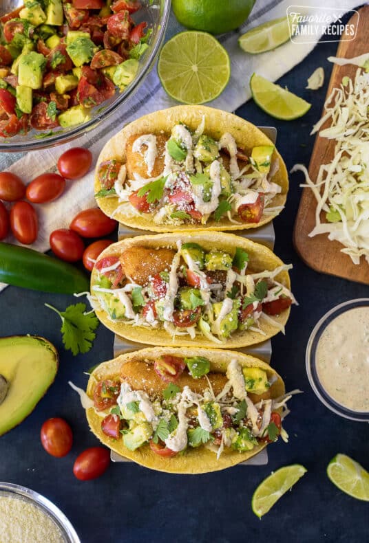 Three Easy Fish Tacos with toppings lined up on a taco stand.