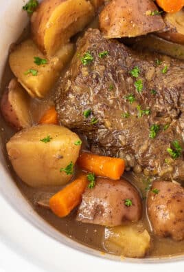 Fork shredding Crockpot Roast Beef surrounded by cooked carrots and red potatoes.