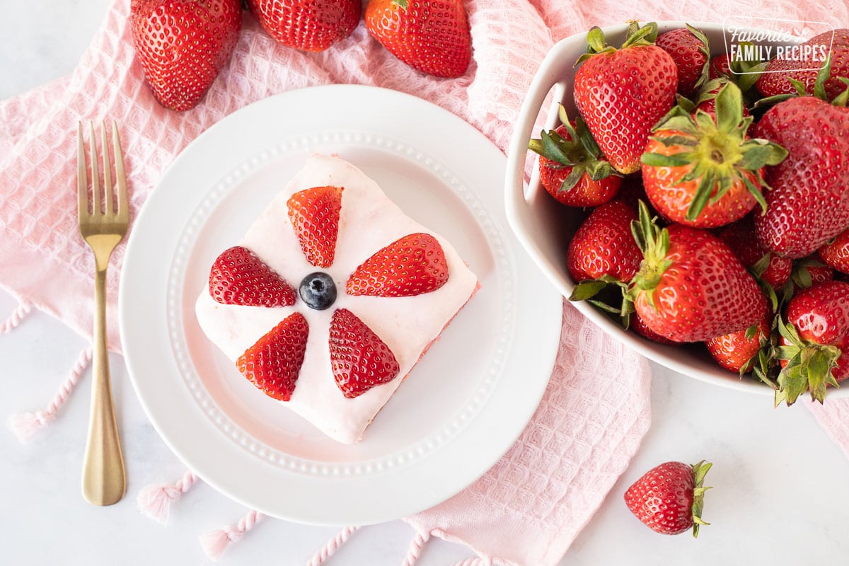 Plate of Fresh Strawberry Cake slice with strawberries and a blueberry.