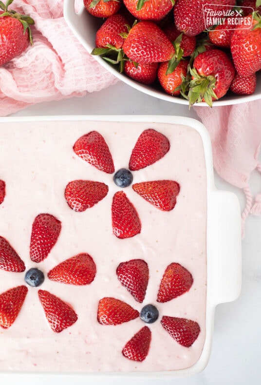 Bowl of fresh strawberries and a baking dish with decorated Fresh Strawberry Cake.