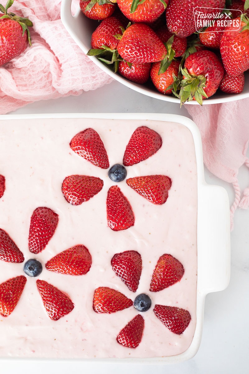 Bowl of fresh strawberries and a baking dish with decorated Fresh Strawberry Cake.