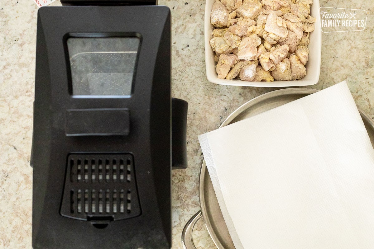 Fryer, battered chicken and a pan with paper towels to make Orange Chicken.