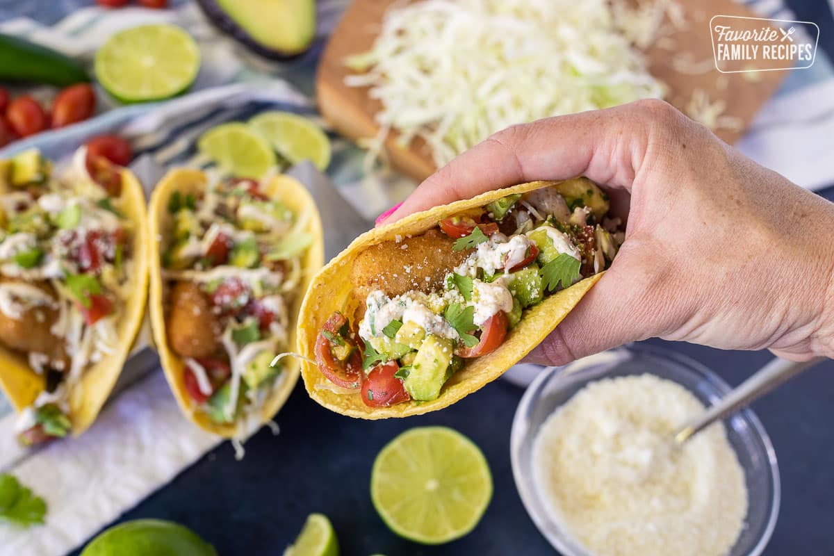 Hand holding an easy Fish Taco topped with pico, cheese, sauce and cilantro.