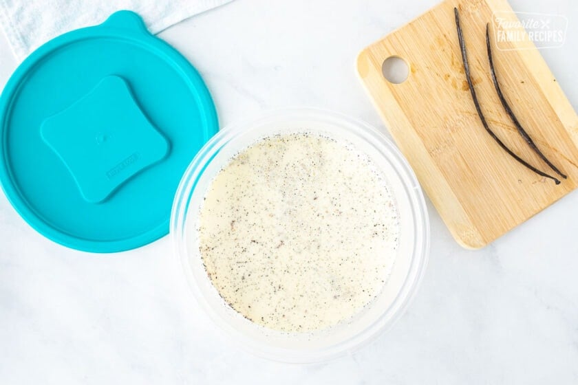 Plastic container with warm Homemade Vanilla Ice Cream mixture. Discarded vanilla beans on the side.