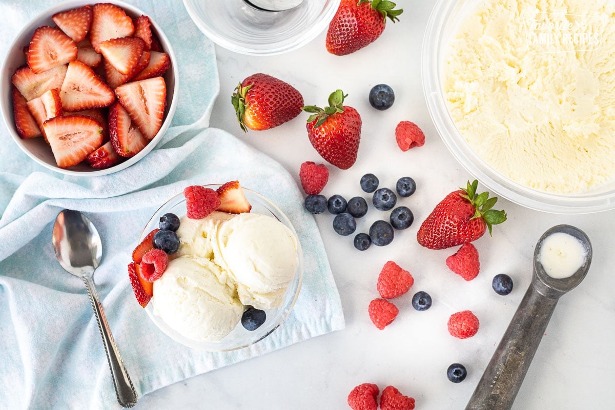 Container of Homemade Vanilla Ice Cream next to fresh berries and a small bowl of scooped ice cream.