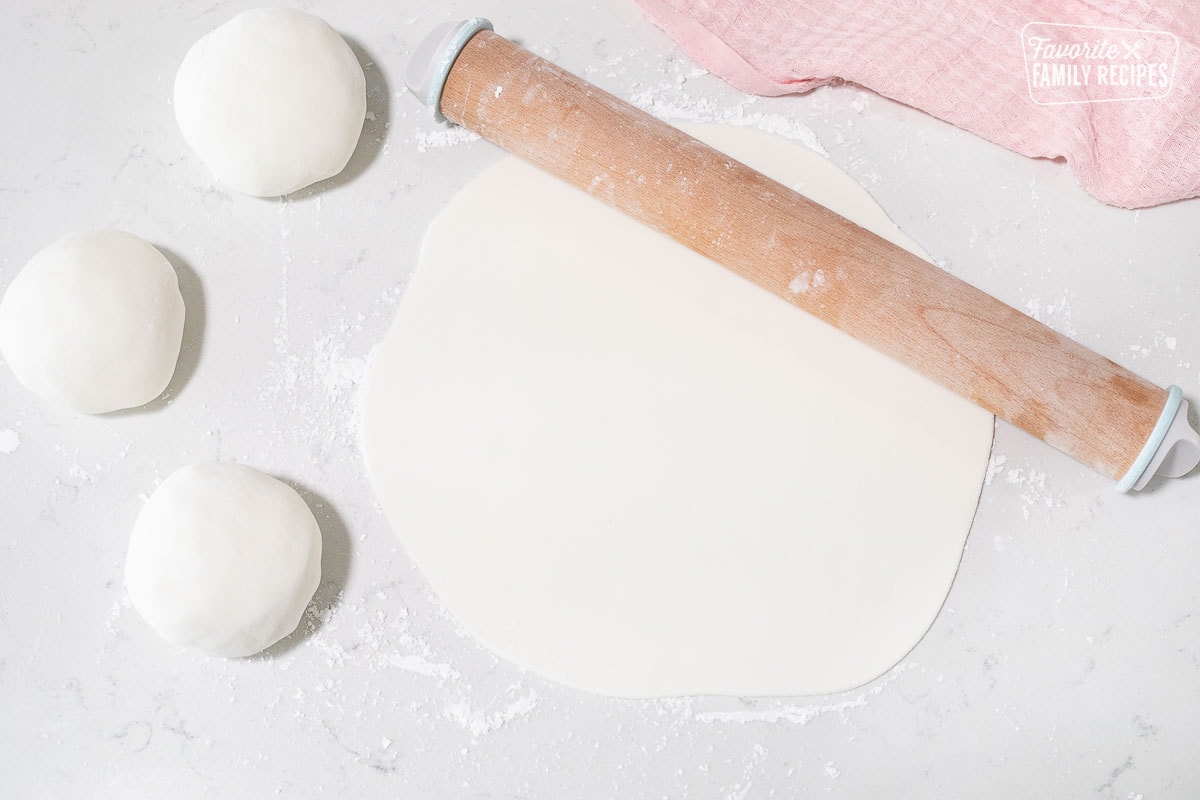 Rolling pin next to three balls of fondant and a flattened out sheet of fondant.
