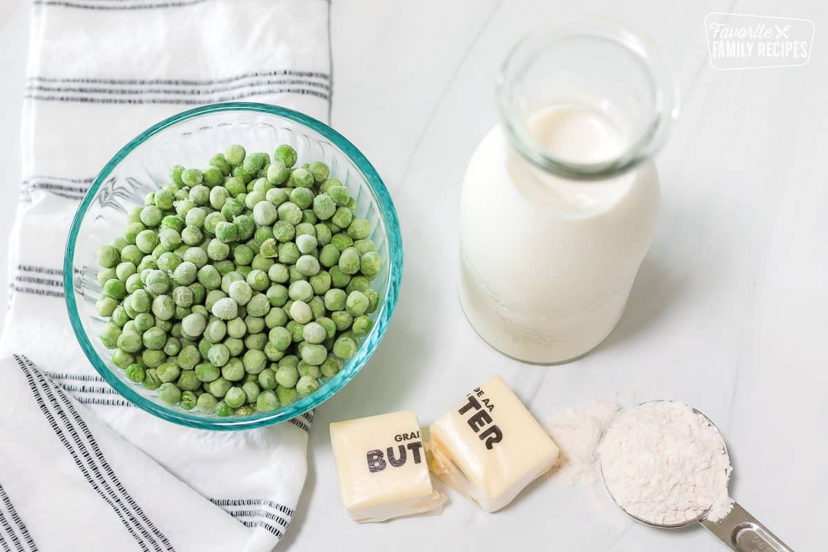Frozen peas in a glass bowl next to butter, milk, and flour.