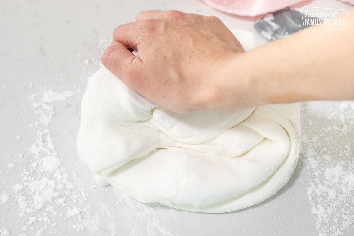 Hand kneading a ball of Fondant with powdered sugar to show How to Make Fondant.