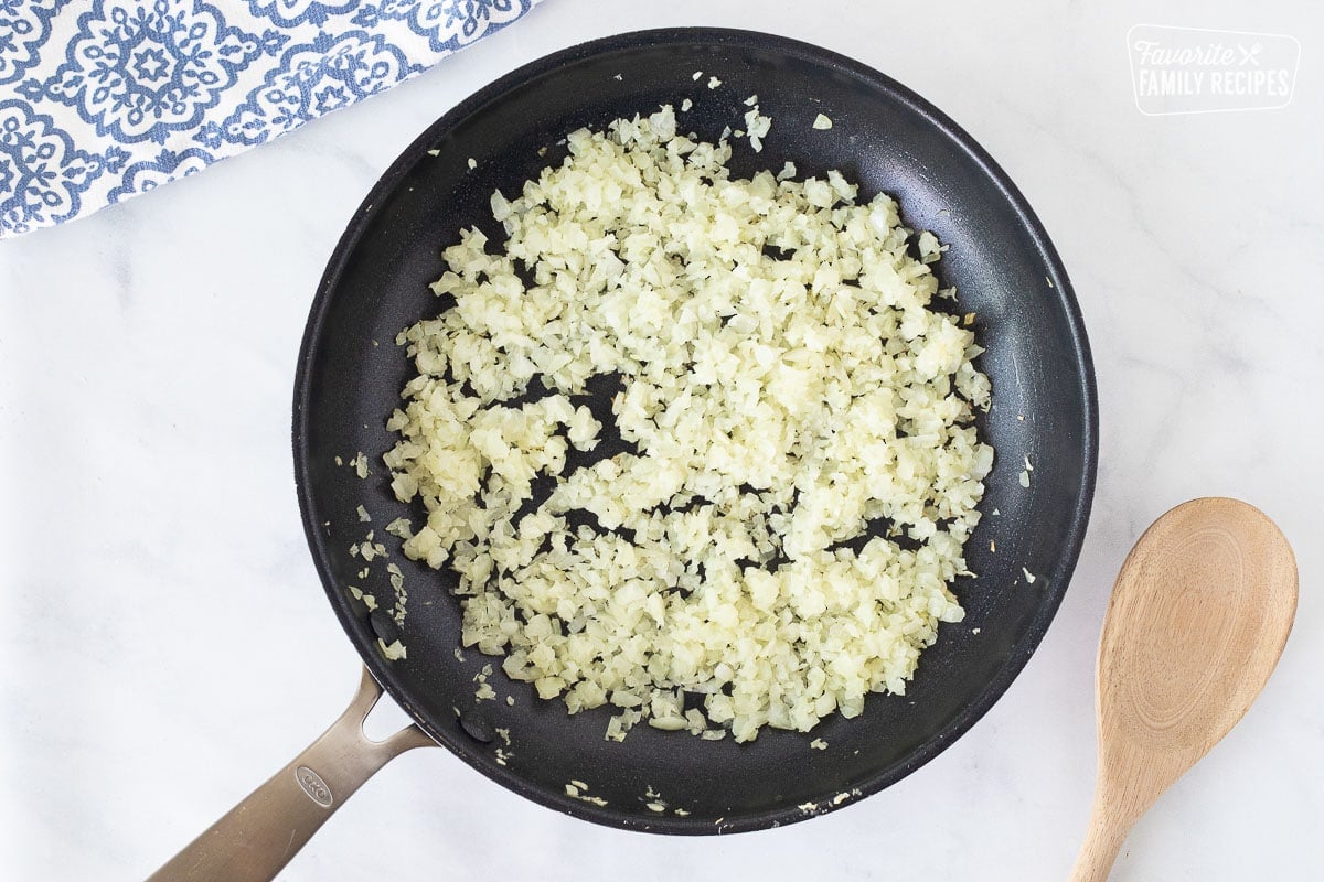 Skillet with sautéed onions for Honey Lime Chicken Enchiladas. Wooden spoon on the side.