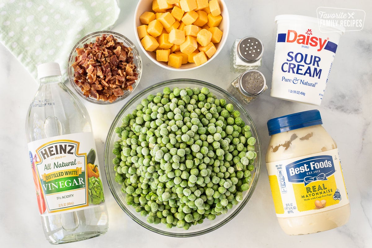 Ingredients to make Green Pea Salad including bacon, cheese cubes, salt, pepper, vinegar, mayonnaise, sour cream and frozen peas.
