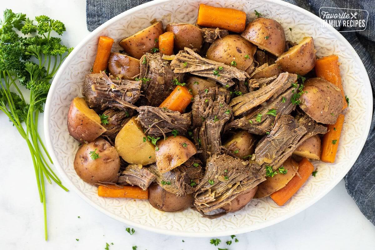 Platter of shredded Slow Cooker Pot Roast with carrots and cut red potatoes.