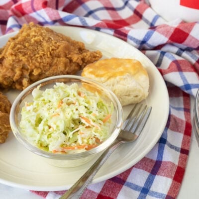 Plate with two pieces of fried chicken, bowl of Coleslaw and a biscuit.