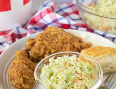 Plate with Coleslaw, chicken and a biscuit. Bowl of coleslaw next to the plate.