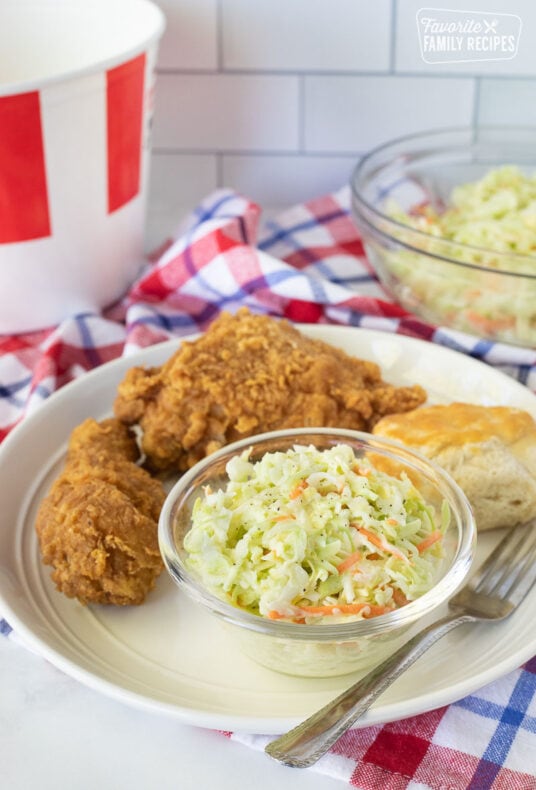 Plate with Coleslaw, chicken and a biscuit. Bowl of coleslaw next to the plate.