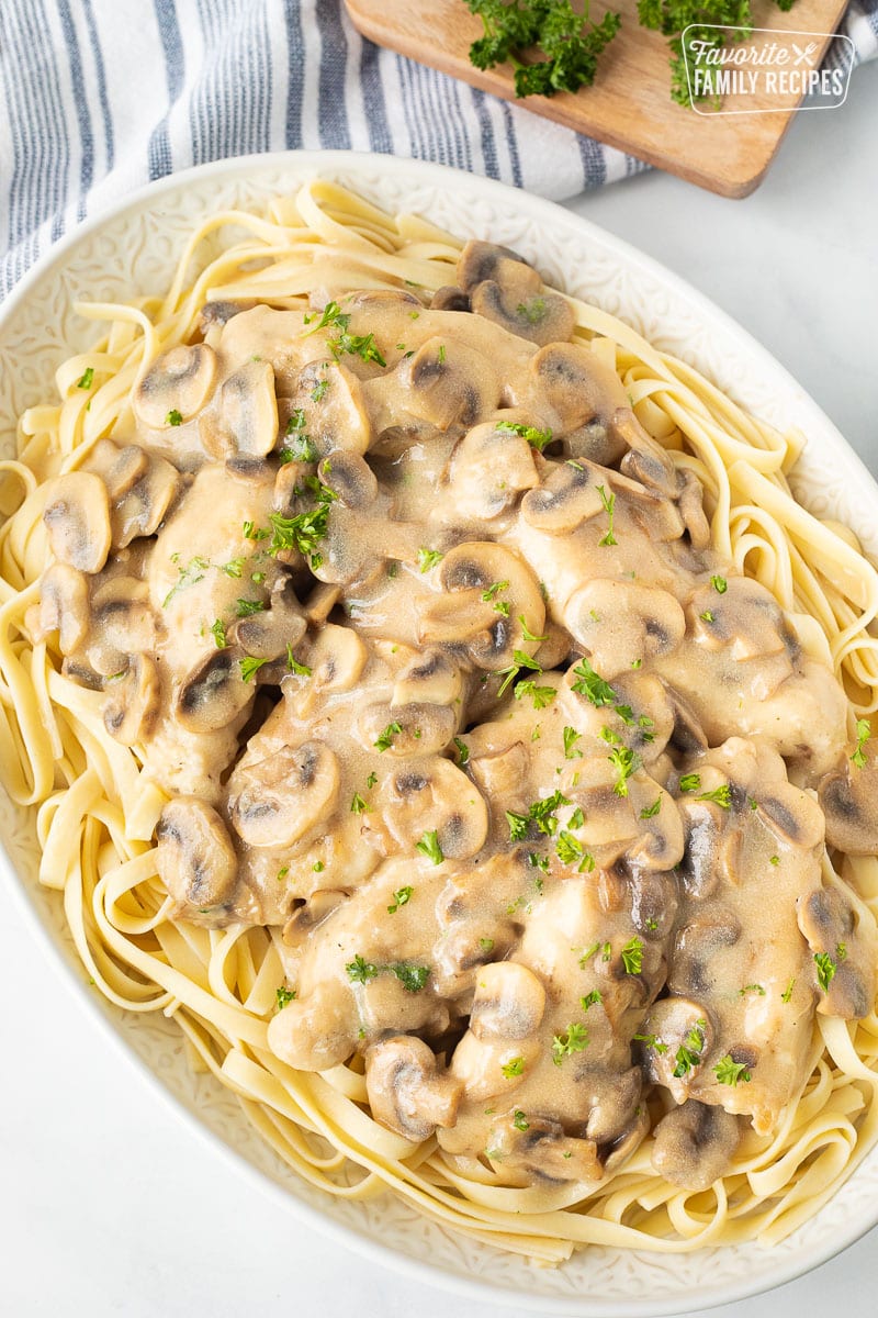 Platter of fettuccine topped with Chicken Marsala and garnished with parsley.