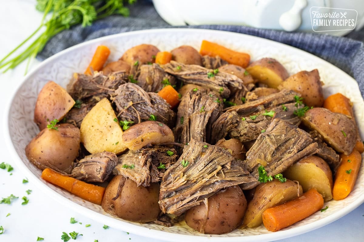 Tender Crockpot Roast Beef on a platter with cooked carrots and potatoes.