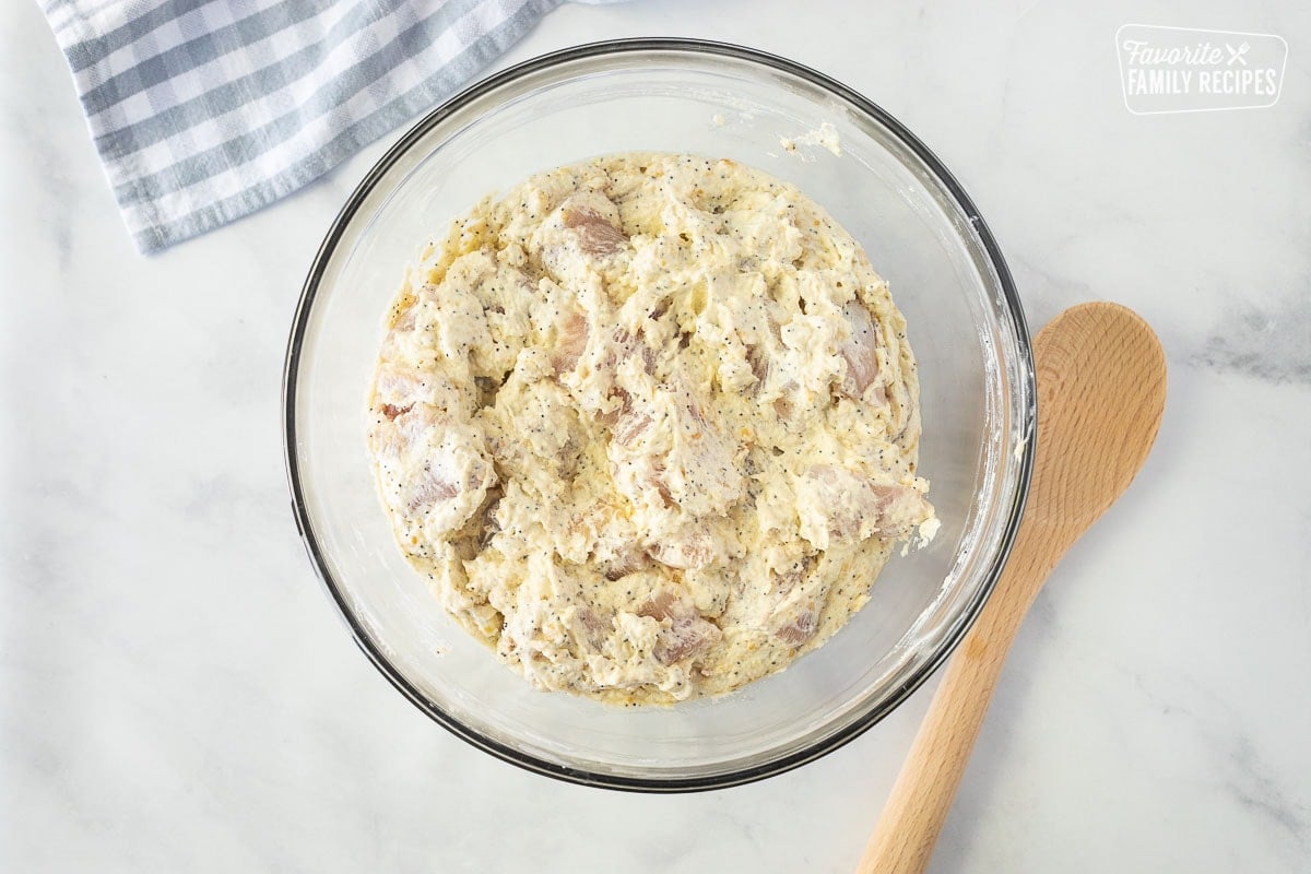 Glass bowl with combined mixture of cup up chicken breasts, sour cream, cream of chicken, crushed Ritz crackers and poppy seeds. Wooden spoon on the side.