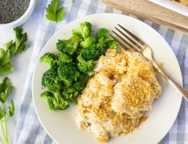 Serving of Poppy Seed Chicken on a plate next to broccoli. Parsley on the side.