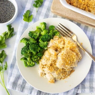 Serving of Poppy Seed Chicken on a plate next to broccoli. Parsley on the side.