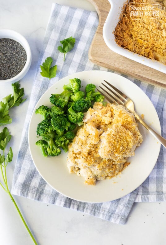Serving of Poppy Seed Chicken on a plate next to broccoli. Parsley on the side.