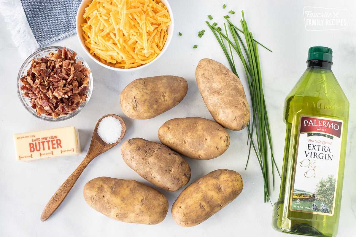 Ingredients to make Potato Skins including potatoes, chives, bacon, cheese, butter, salt and olive oil.