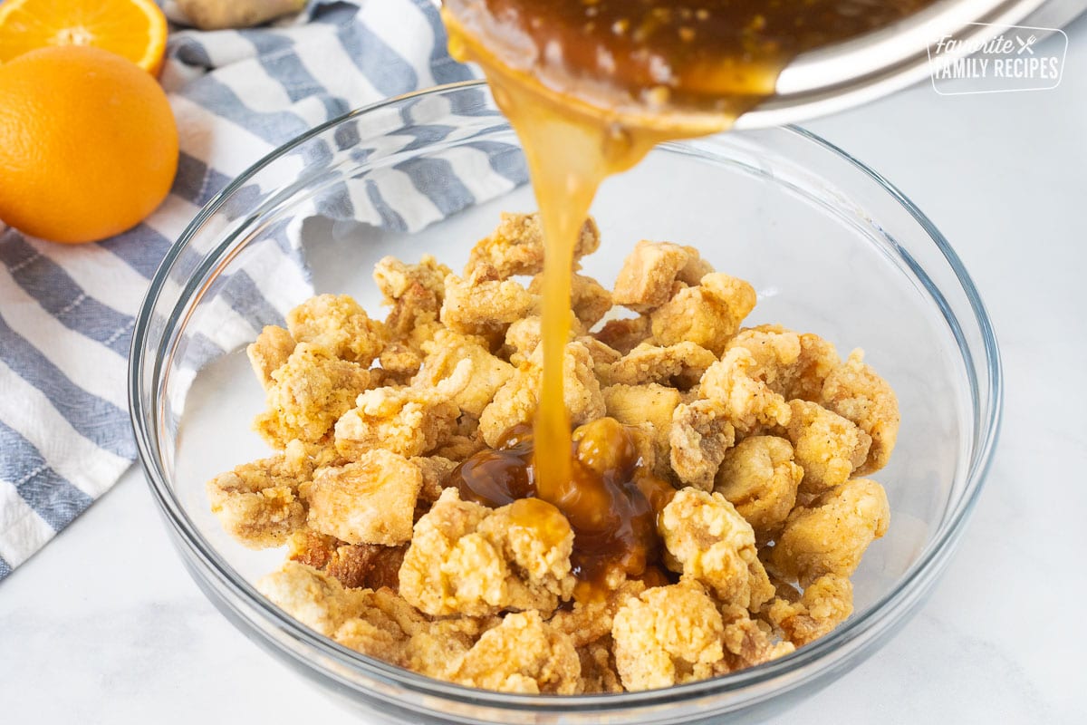 Sauce pouring onto fried chicken for Orange Chicken.