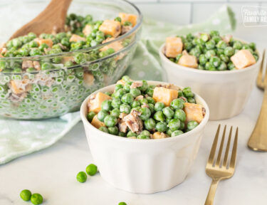Serving bowls full of Green Pea Salad with forks.